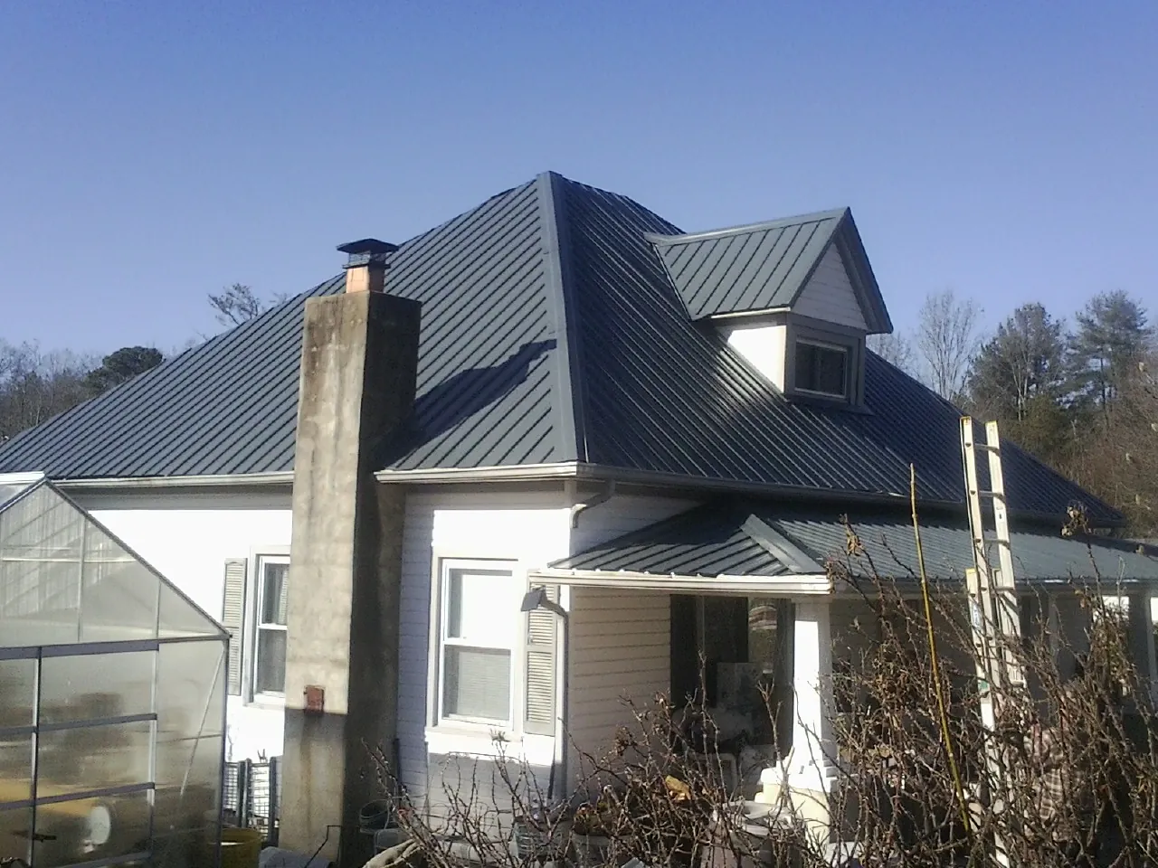 Dark blue standing seam metal roof on a white farmhouse with dormer — Slate & Tile Roof Repair by Roofing Brothers in New Athens
