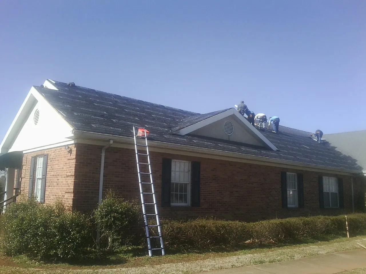 Crew tearing shingles off a brick ranch roof with a ladder set — Emergency Roof Repair work by our crew in New Athens