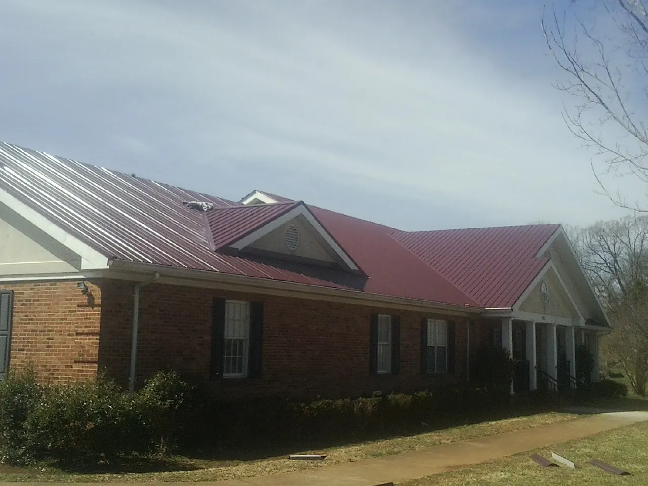 Red metal roof with gabled entries on a long brick building, from a Hail Damage Roof Repair job in New Athens