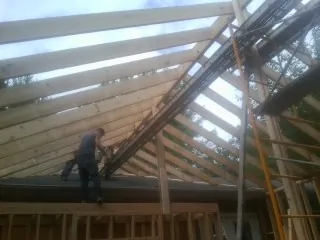 Rafters going up over a new addition with a worker on the wall in New Athens