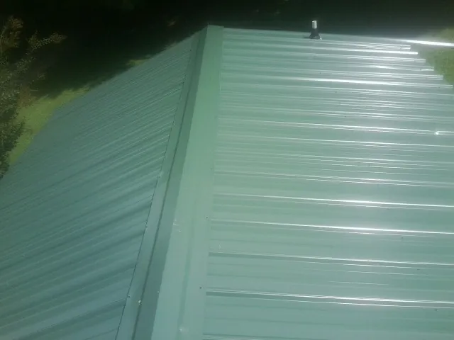 New green metal panels meeting at the ridge of a roof — Flat Roof Repair work by our crew in New Athens