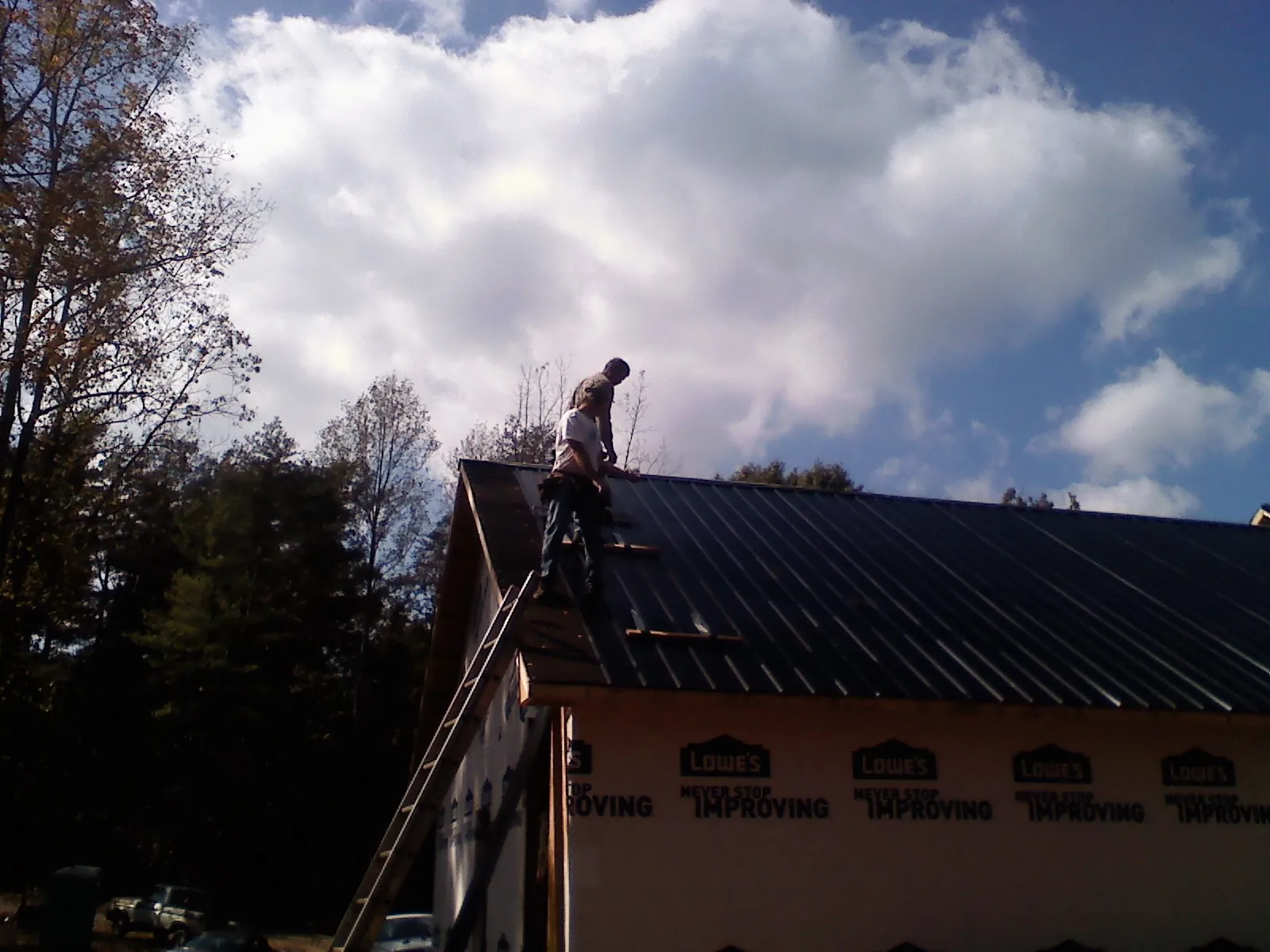 Roofer fastening dark metal panels high against a cloudy sky, from a Roof Inspection job in New Athens