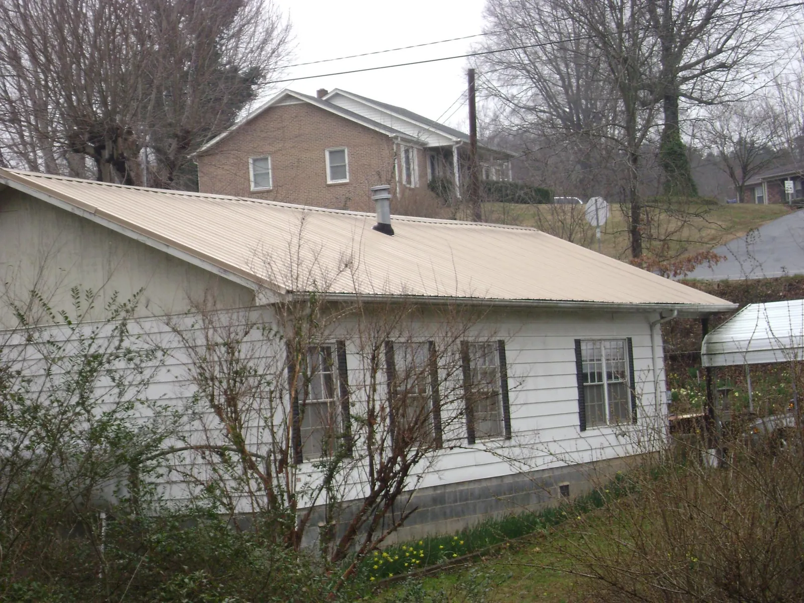 Tan metal roof on a white sided house set into a hillside — Commercial Roofing by Roofing Brothers in New Athens