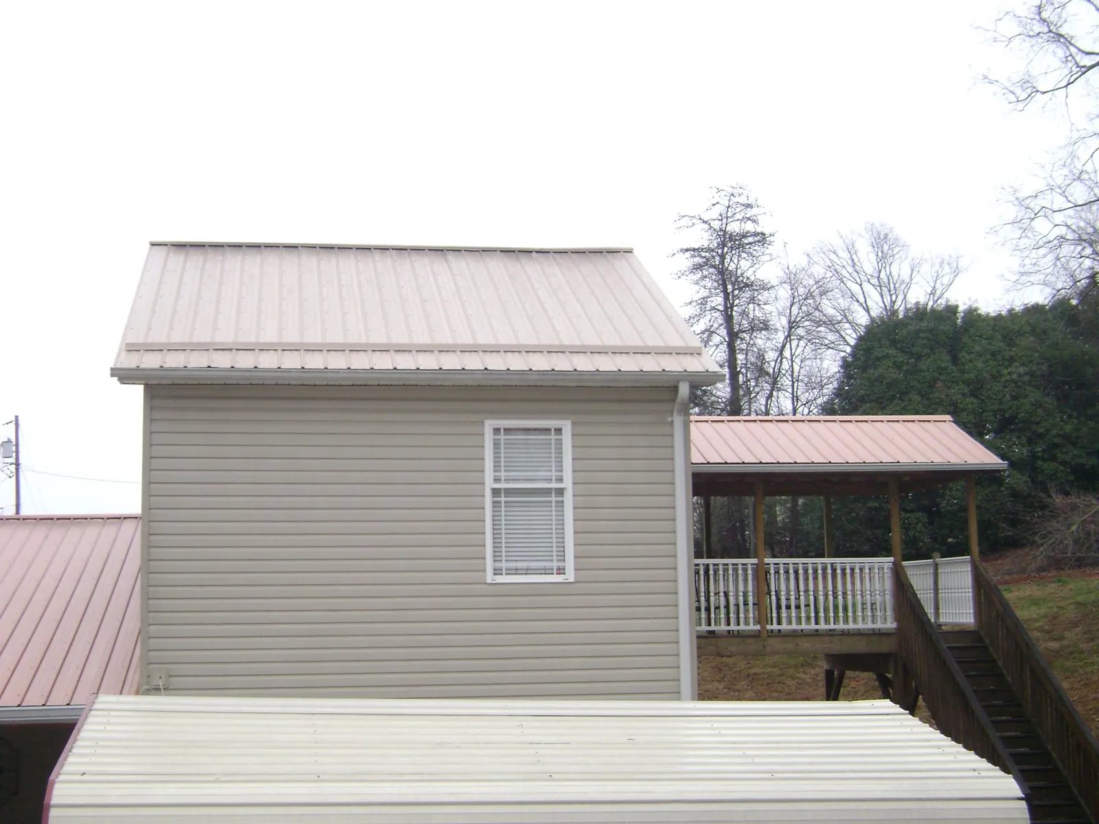Tan metal roofs on a two story addition and attached porch, from a Roof Replacement job in New Athens